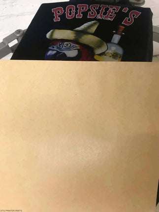 Kraft Dark Garment Pressing Paper 16" x 20" on dark fabric, bold red letters above a yellow hat and blue parrot graphic.