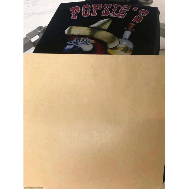 Kraft Dark Garment Pressing Paper 16" x 20" on dark fabric, bold red letters above a yellow hat and blue parrot graphic.